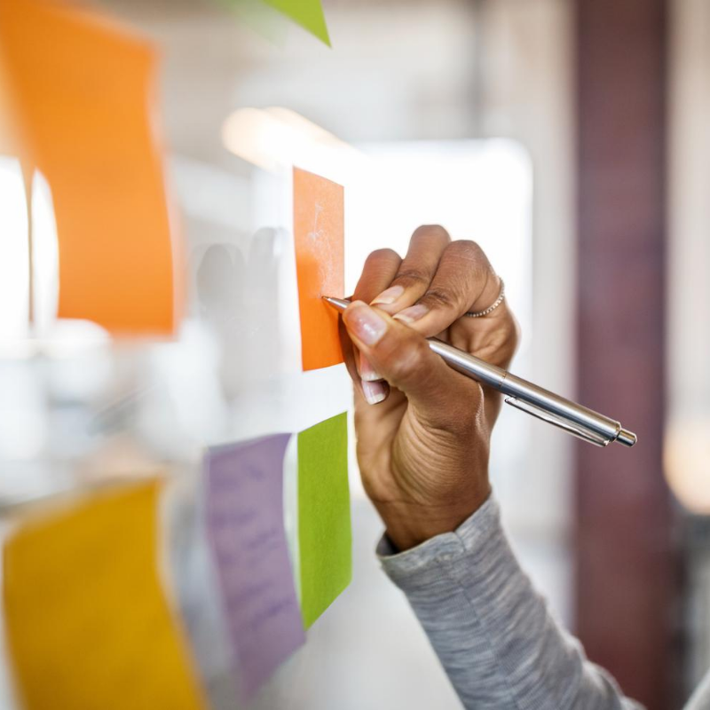 Business man hand writing on colored sticky note paper on white board background